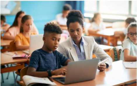 Teacher guiding a student on a laptop in a classroom, representing modern education methods in higher education. Perfect for Education Eureka articles on innovative teaching practices.