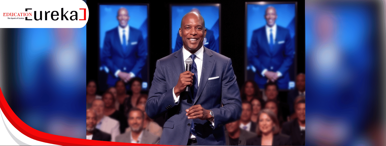 Eric Bailey speaking at a motivational event with a live audience and his image on large screens behind.