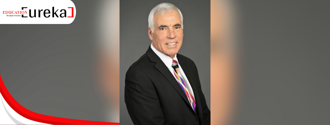Ken Keis in a professional black suit and multicolored tie, smiling confidently against a grey backdrop.