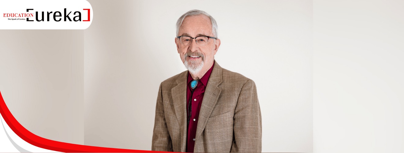 Richard Larson, MIT professor, wearing a brown blazer and red shirt, smiling confidently in a neutral-toned background for Education Eureka 2025.